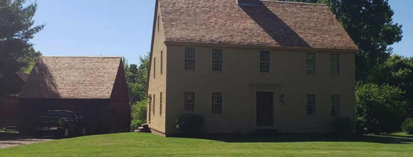 Saltbox home with yellow siding and brick chimney.
