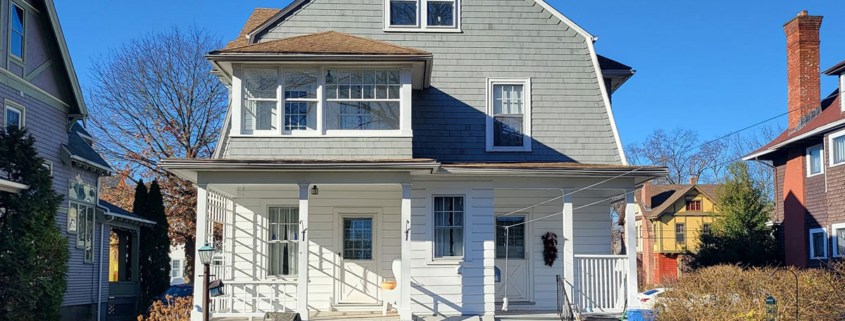 A two-story house with gray shingle siding on the upper level, white horizontal lap siding below, and a gabled roof.