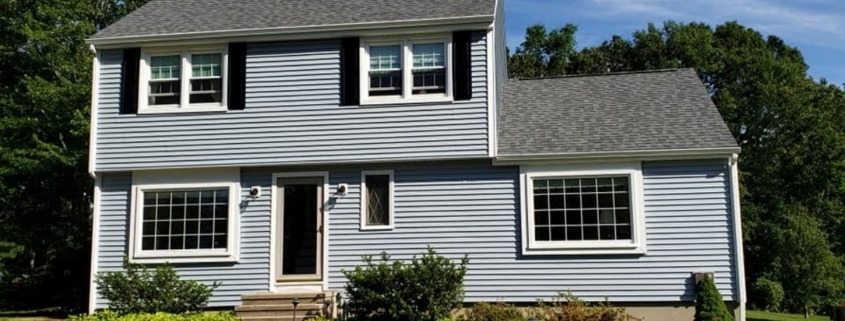 Exterior of a two-story house with blue horizontal lap siding, black shutters on the upper windows, and white trim around the doors and large lower windows.