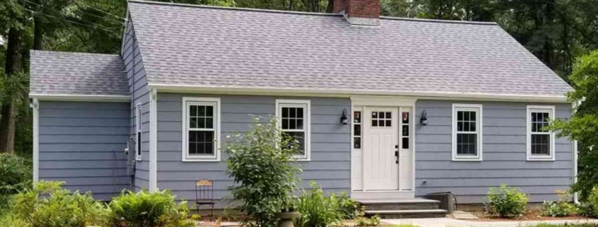 Cottage with blue-gray siding and brick chimney.