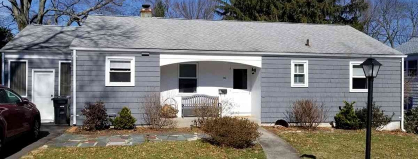 Single-story home with dark gray shingle siding, white trim, and a small arched porch entry.