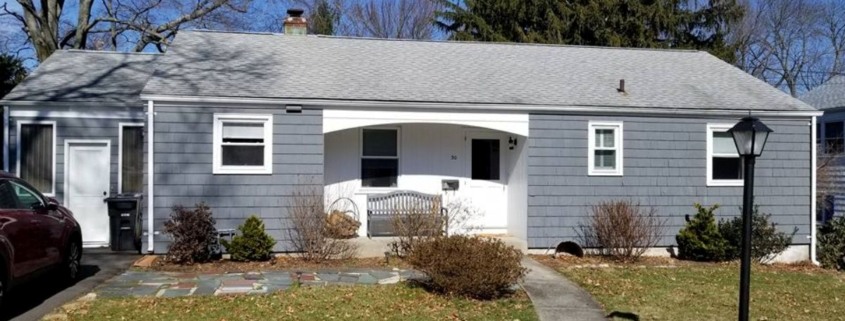 Single-story home with dark gray shingle siding, white trim, and a small arched porch entry.