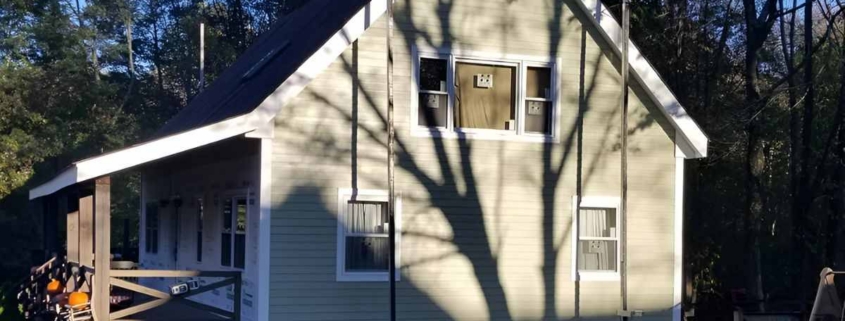 Gabled two-story house with light sage green horizontal siding, white trim, and a side-view porch.