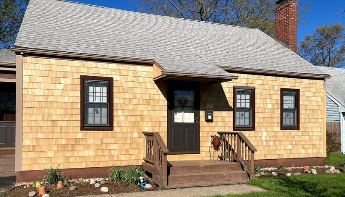 A small house with newly installed wooden shingles and a light gray roof.