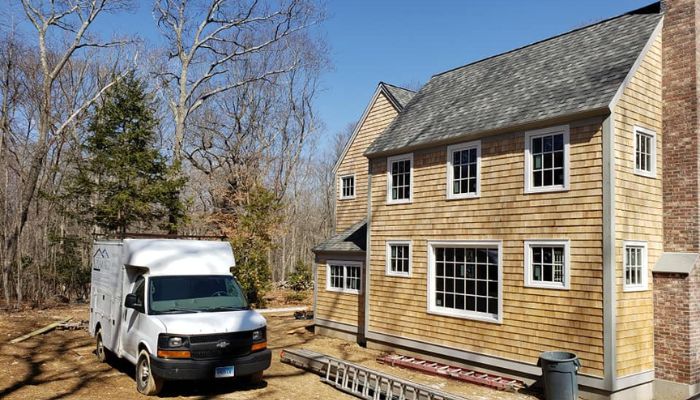 A truck parked beside a shingled house under construction with a ladder leaning against it.