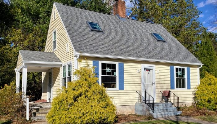 A small yellow house featuring blue shutters, illustrating the roof with code compliance.