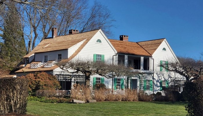A spacious white house with green shutters, illustrating frequent roof repair.