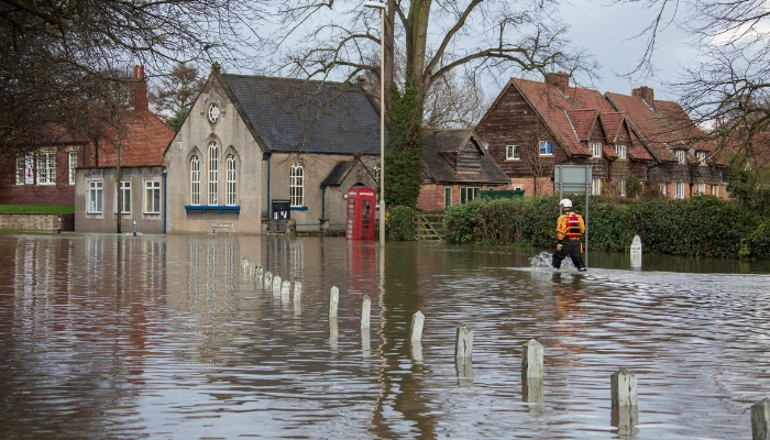 A man wearing a safety vest navigates a flooded street, illustrating the impact of storms on local infrastructure.