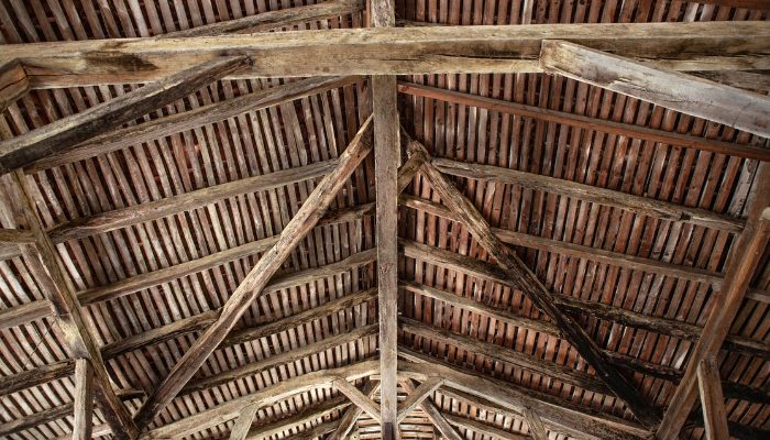 Interior view of an old barn ceiling with wooden beams, illustrating signs of wear and potential structural rot.