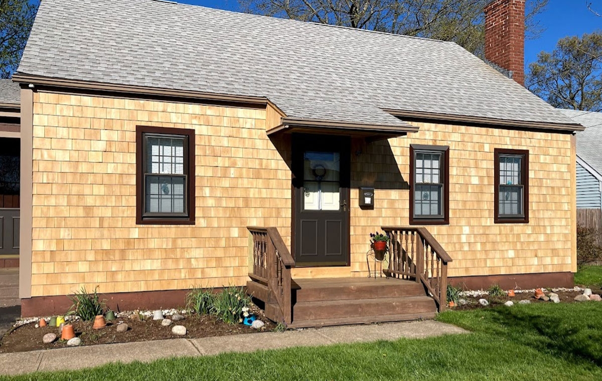 A quaint house featuring brown siding and a black door, representing a charming residential style.