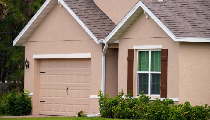 A tan house with brown shutters and a garage door, showcasing stucco siding.