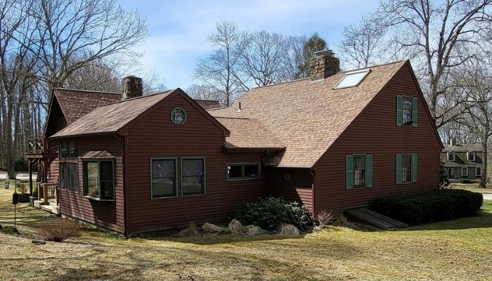 A red house with a brown roof and green trim, illustrating siding options for Connecticut's climate and building codes.