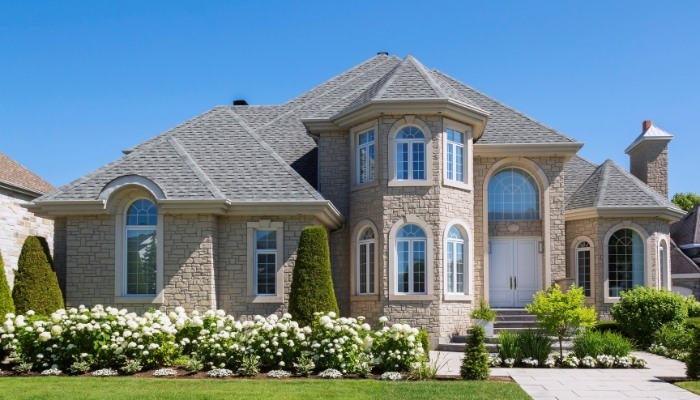 A grand house with elegant stone veneer siding, complemented by a vibrant lawn and attractive landscaping.