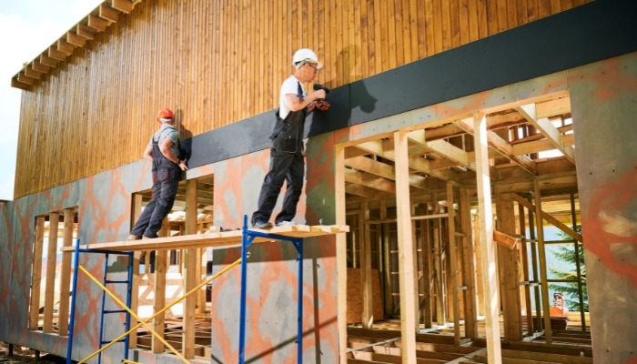 Workers installing siding on house under construction.