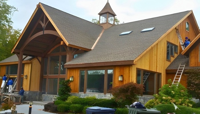 A worker in a yellow high-visibility vest and hard hat installing new light-gray horizontal siding on the exterior of a house.