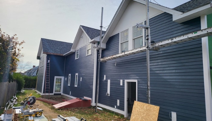 Exterior view of a multi-story house under construction with navy blue horizontal siding, white gables, and metal scaffolding.