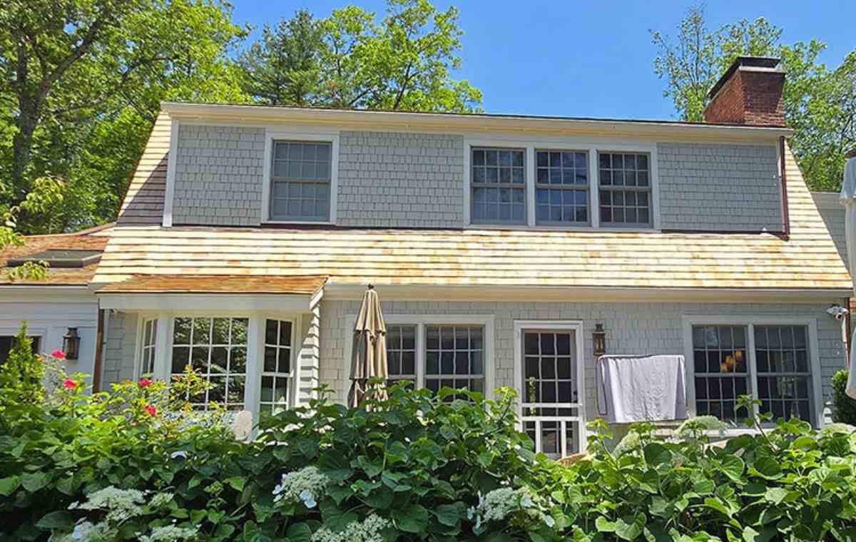 A house with a white shingled roof and fence, showcasing cedar siding, nestled in a tranquil outdoor setting.