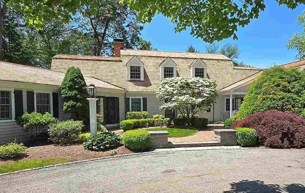 A prominent home with cedar siding, a driveway, and several trees in the landscape.