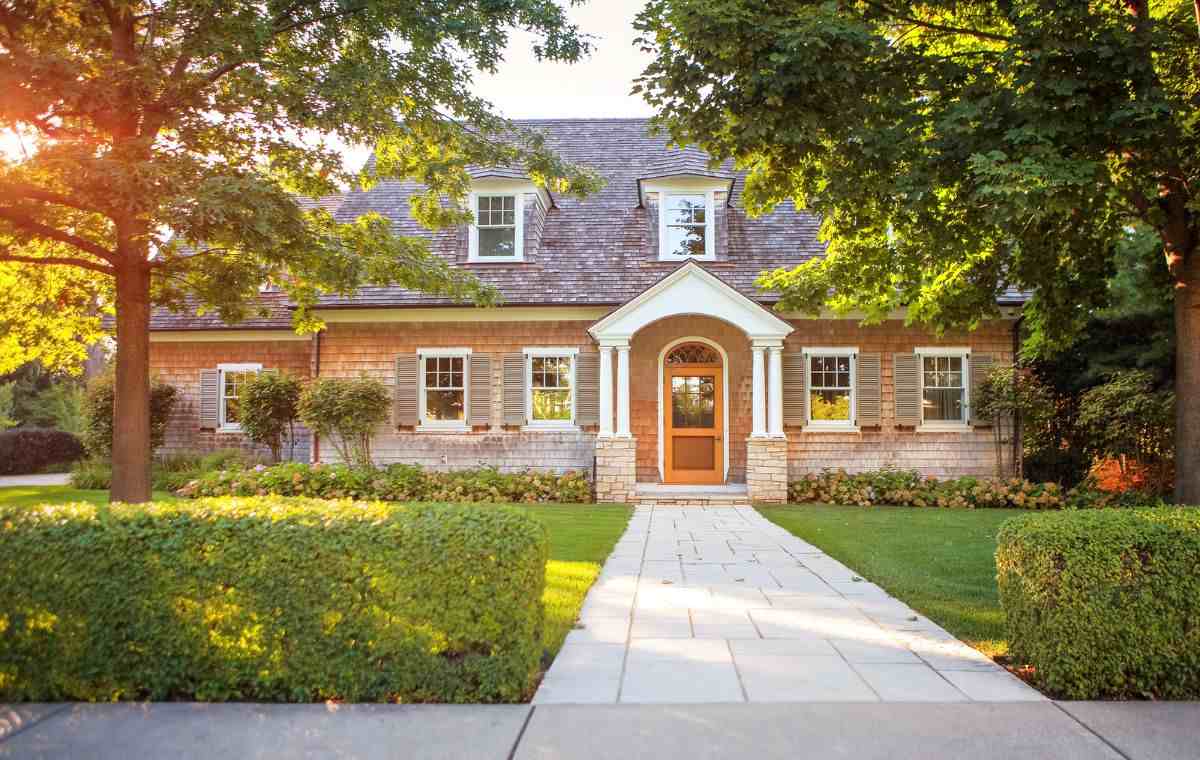 Traditional cedar shingle cottage with a white gabled portico, wood front door, and gray shutters.