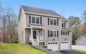 Modern two-story house with gray horizontal lap siding, dark navy blue shutters, and a small white gabled front porch leading to two white garage doors.
