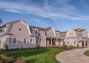 Exterior of a large, gray shingle house featuring multiple gambrel rooflines, white trim, and a gravel driveway.