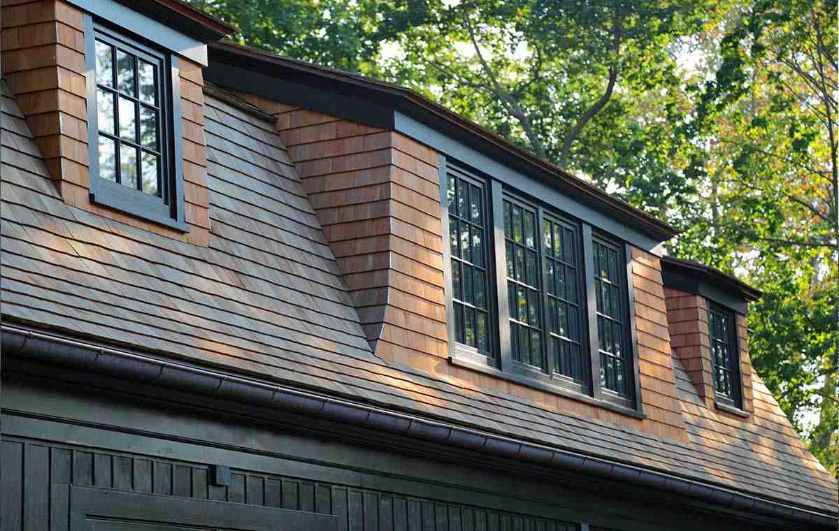 Home with wood shingle roof and dormers surrounded by trees.