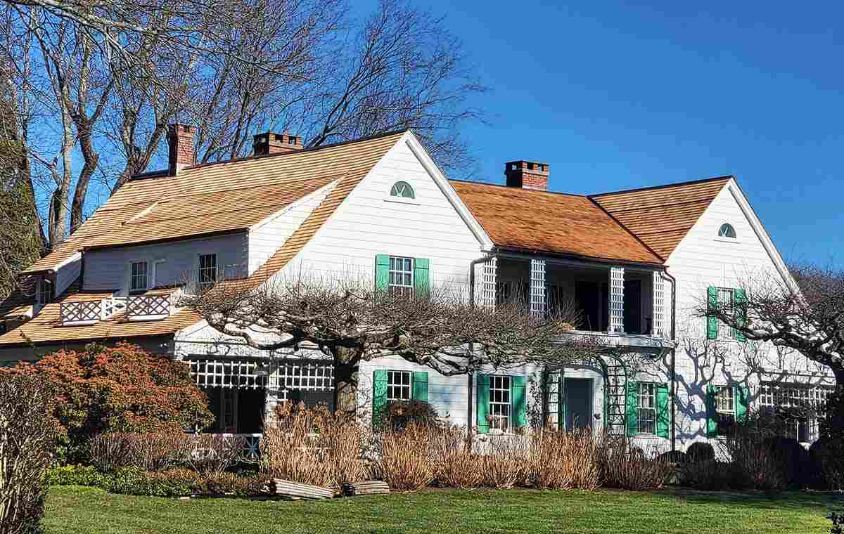 Exterior of a white home with wood shingle roof, gables, and green shutters.
