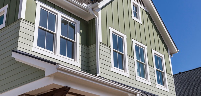 A green house featuring white trim and multiple windows, highlighting its attractive design.