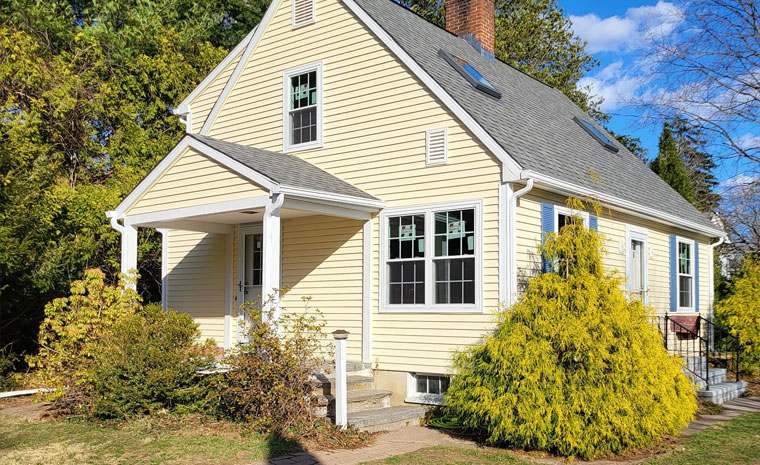 A yellow house with white trim, a black roof, and several windows, set against a clear blue sky.