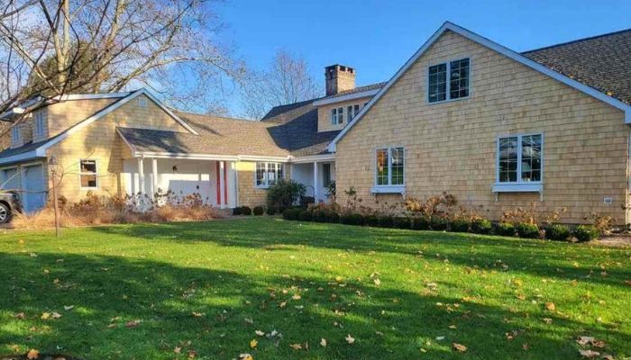 A large suburban home with tan cedar shake siding, a green lawn, and multi-pane windows.