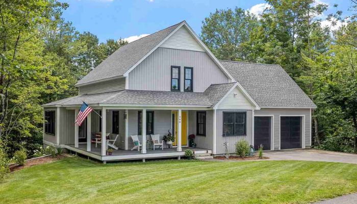 A gray house featuring vertical and horizontal Hardie siding, a wrap-around porch, and a garage.