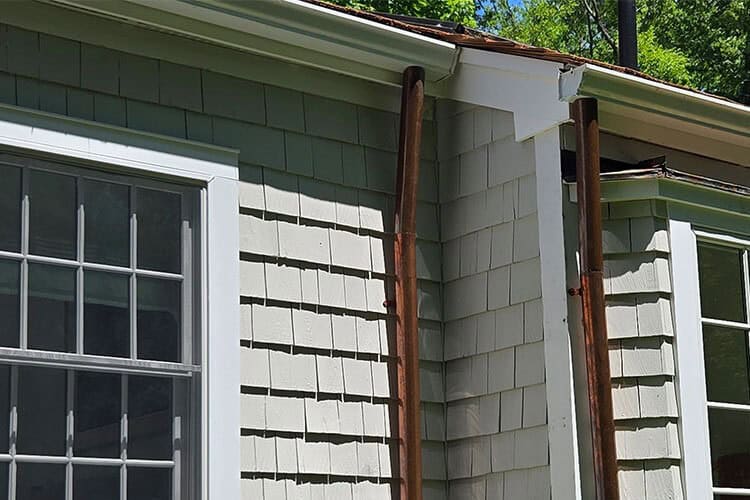 Copper downspouts on a light gray shingle house with white-trimmed gutters and windows.