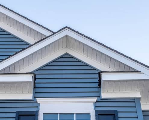 Close-up of a house roofline featuring blue siding, white gables, and trim.