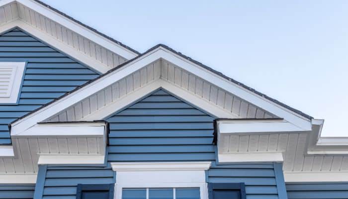 Close-up of a house roofline featuring blue siding, white gables, and trim.
