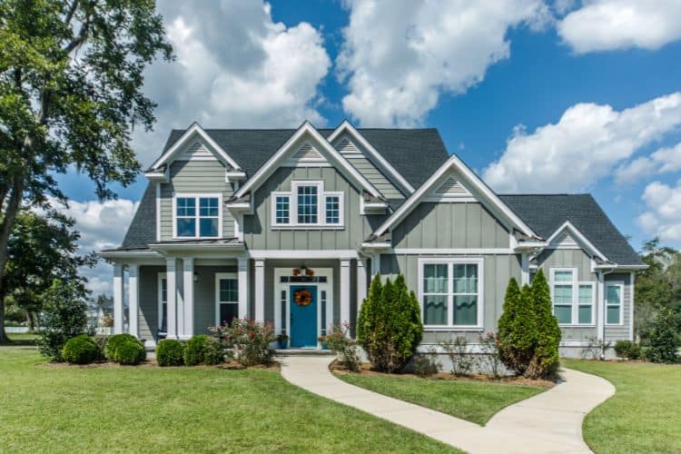 Two-story sage green house with white trim, a blue front door, and a curved walkway.