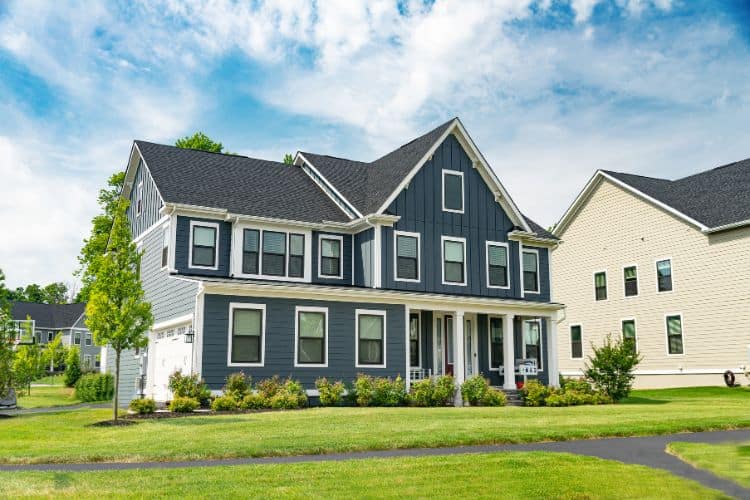 Two-story dark blue house with white trim, a covered front porch, and a green lawn.