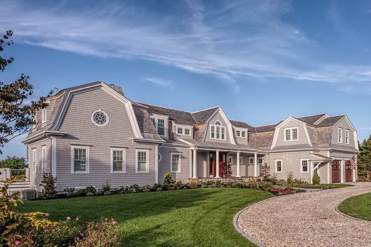 Grey wood shingle siding on a large coastal house with gambrel rooflines and white trim.