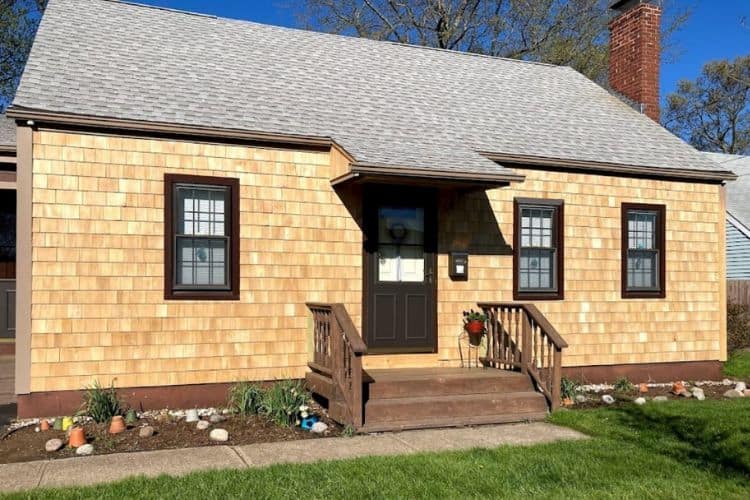 Light cedar shake siding on a small home exterior with brown window frames and porch steps.